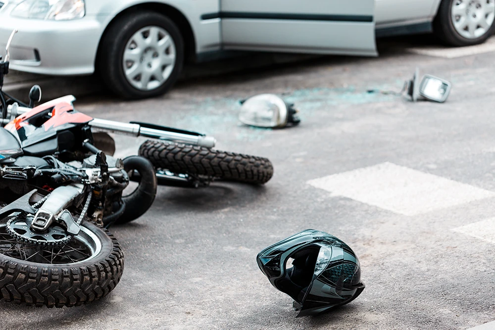 Overturned motorcycle and helmet on the road beside a car after a collision